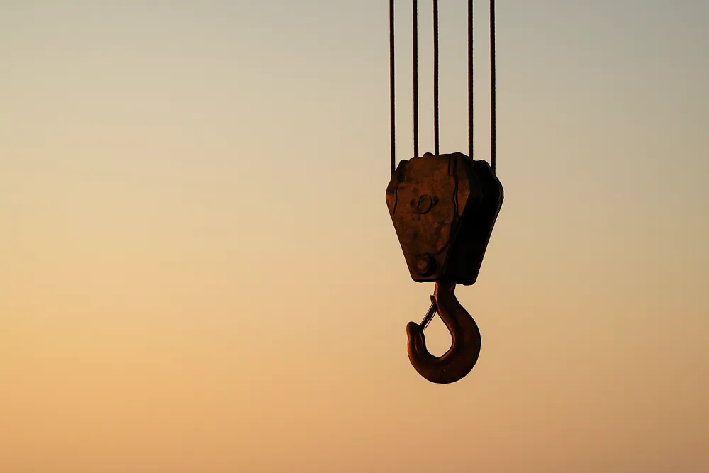 A tower crane hook and cables hanging against a pale evening sky — sunset clauses, Baulkham Hills. Illustrative example.